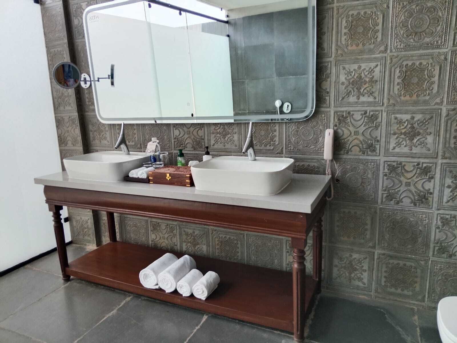 A bathroom with a double sink, a mirror above, a towel rack, and decorative wall tiles.