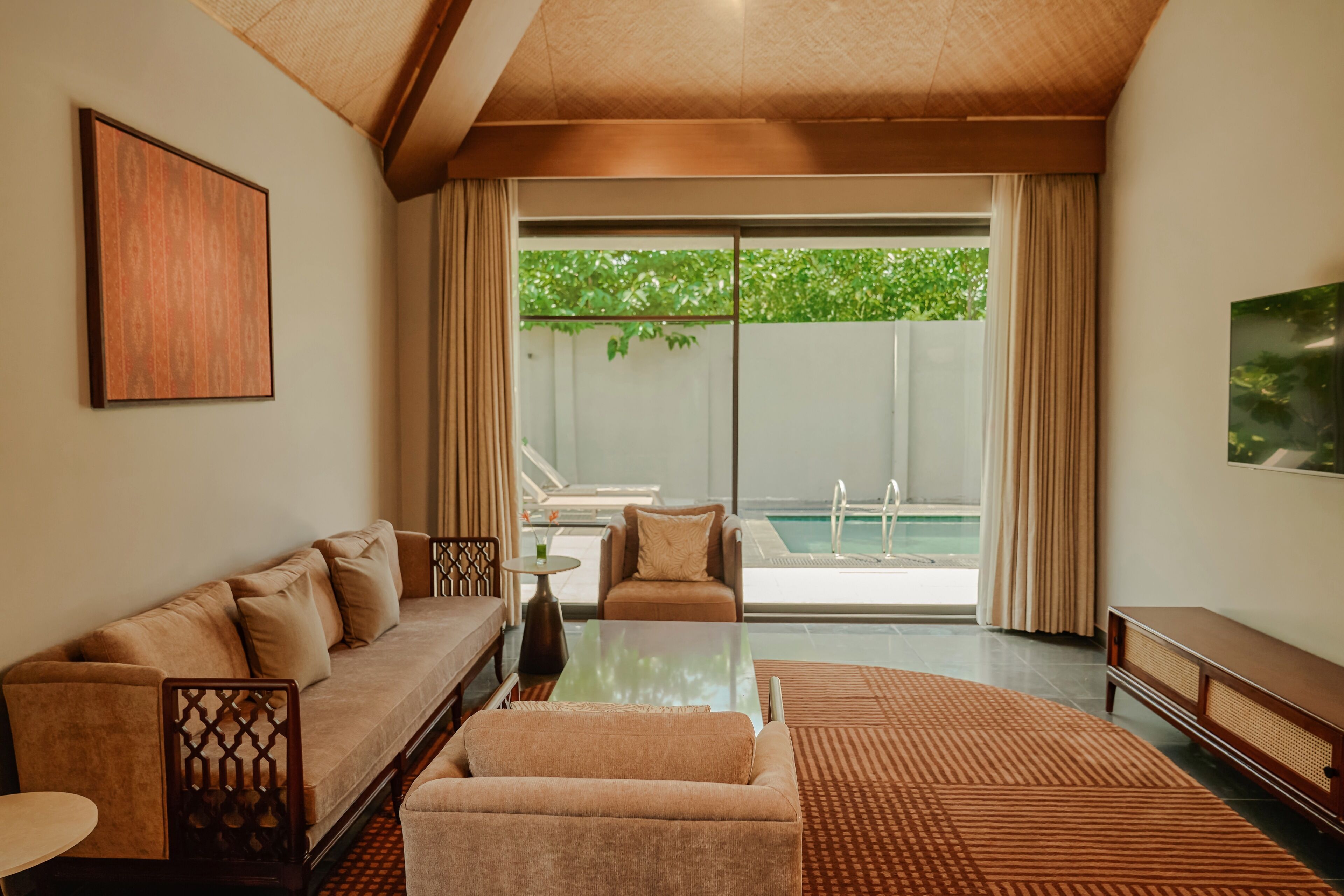 A modern living room with a sofa, a coffee table, and a view of a pool through large sliding doors.