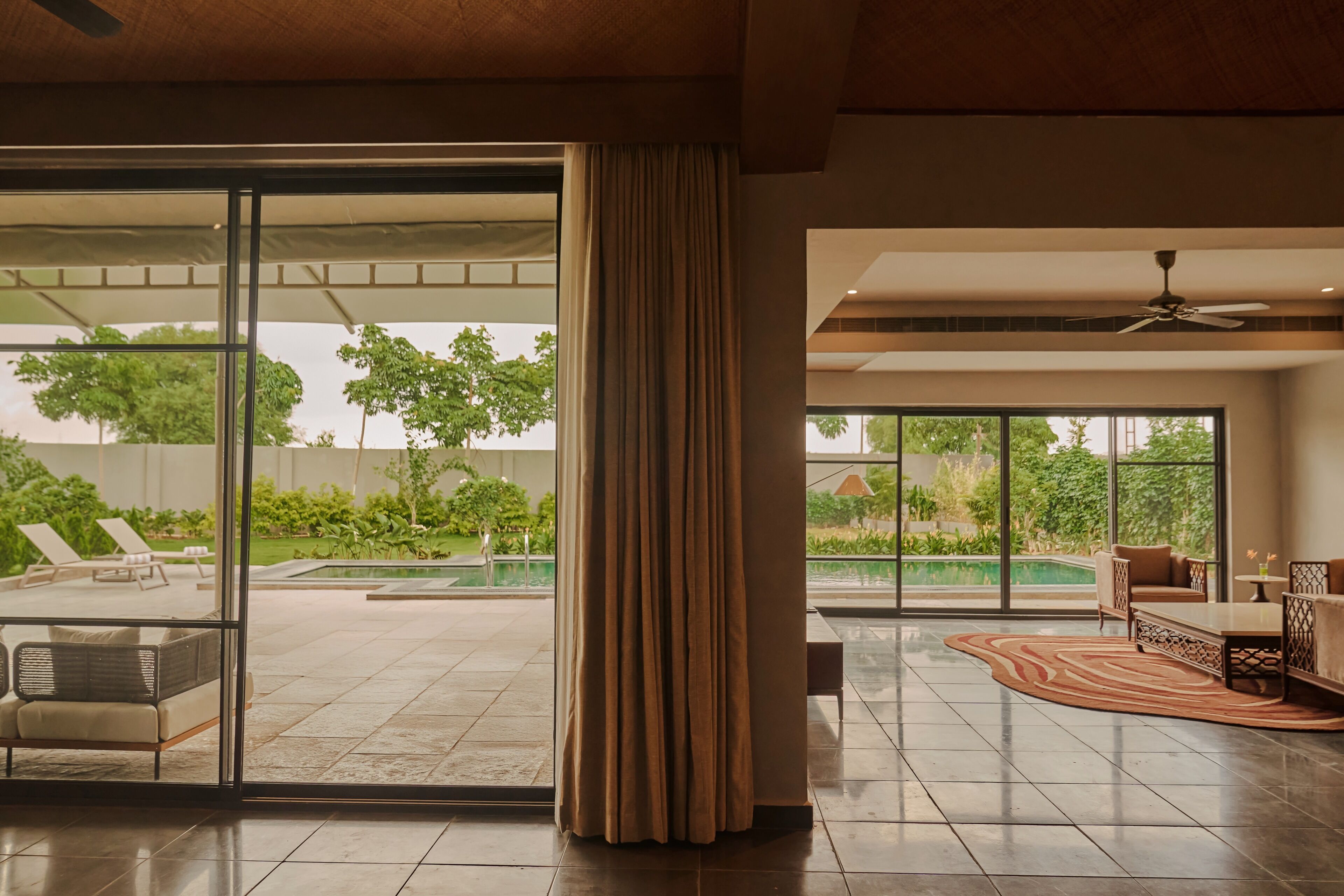 A spacious indoor area with a large sliding glass door leading to an outdoor pool area, a ceiling fan, and a seating area with a patterned rug.