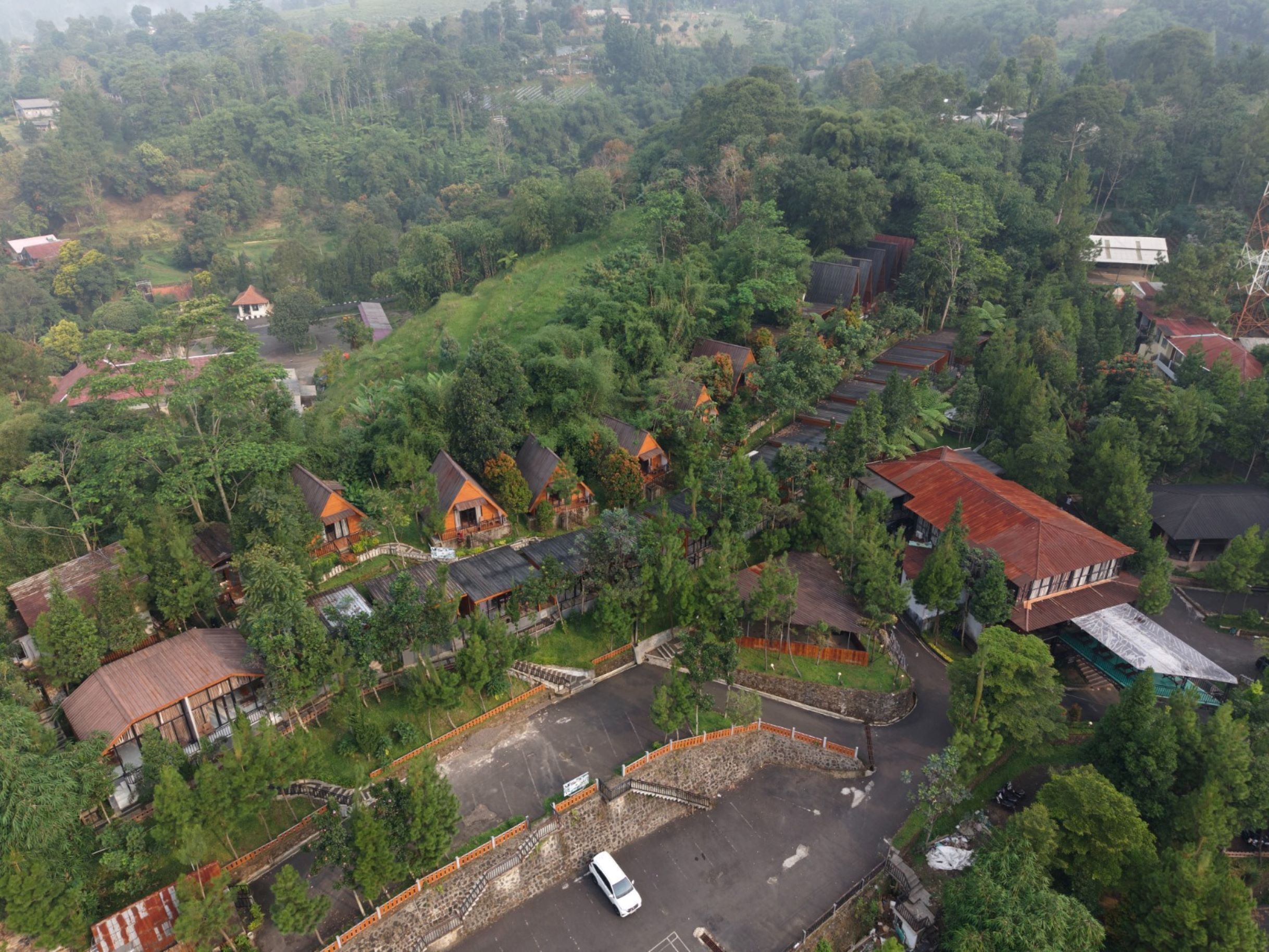 A residential area with multiple houses, some with sloped roofs, surrounded by dense greenery.