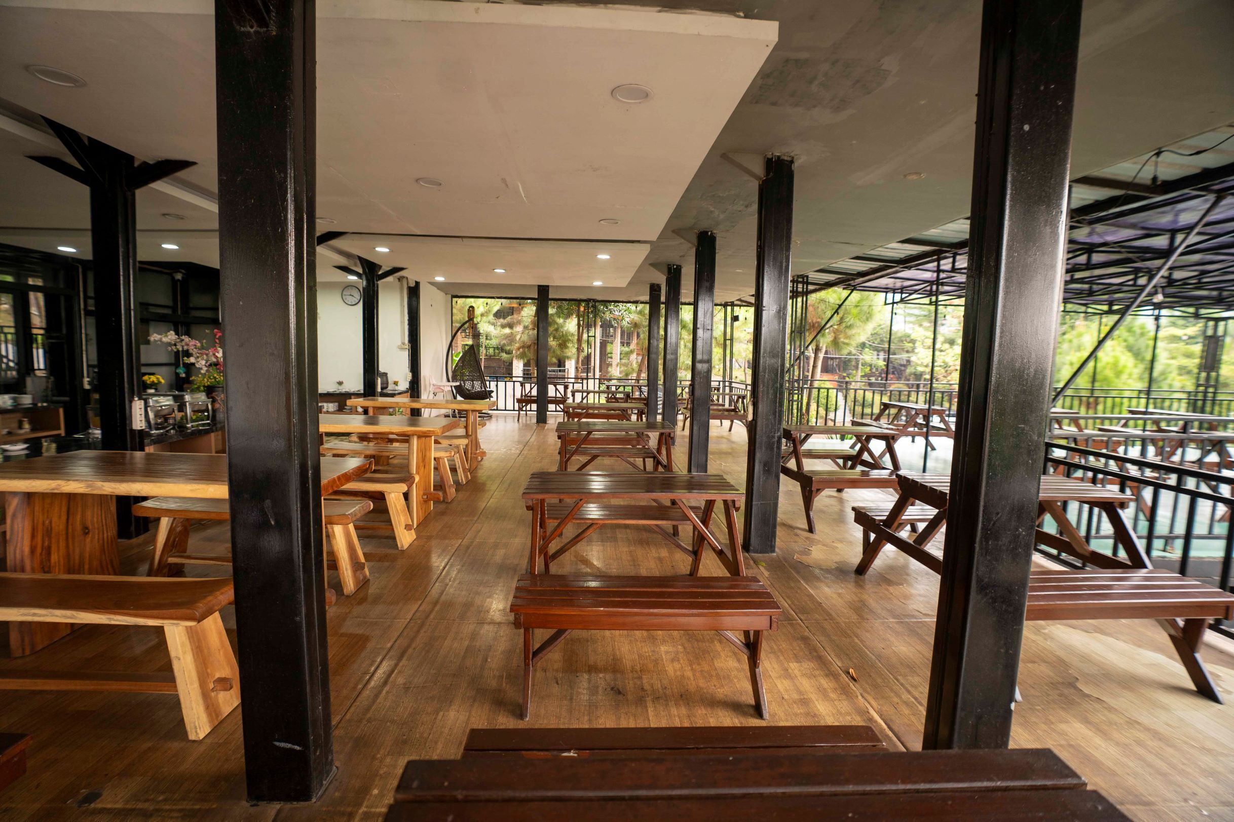 Un comedor interior con mesas y bancos de madera, techo alto y vistas al exterior.