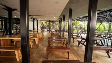 Un comedor interior con mesas y bancos de madera, techo alto y vistas al exterior.