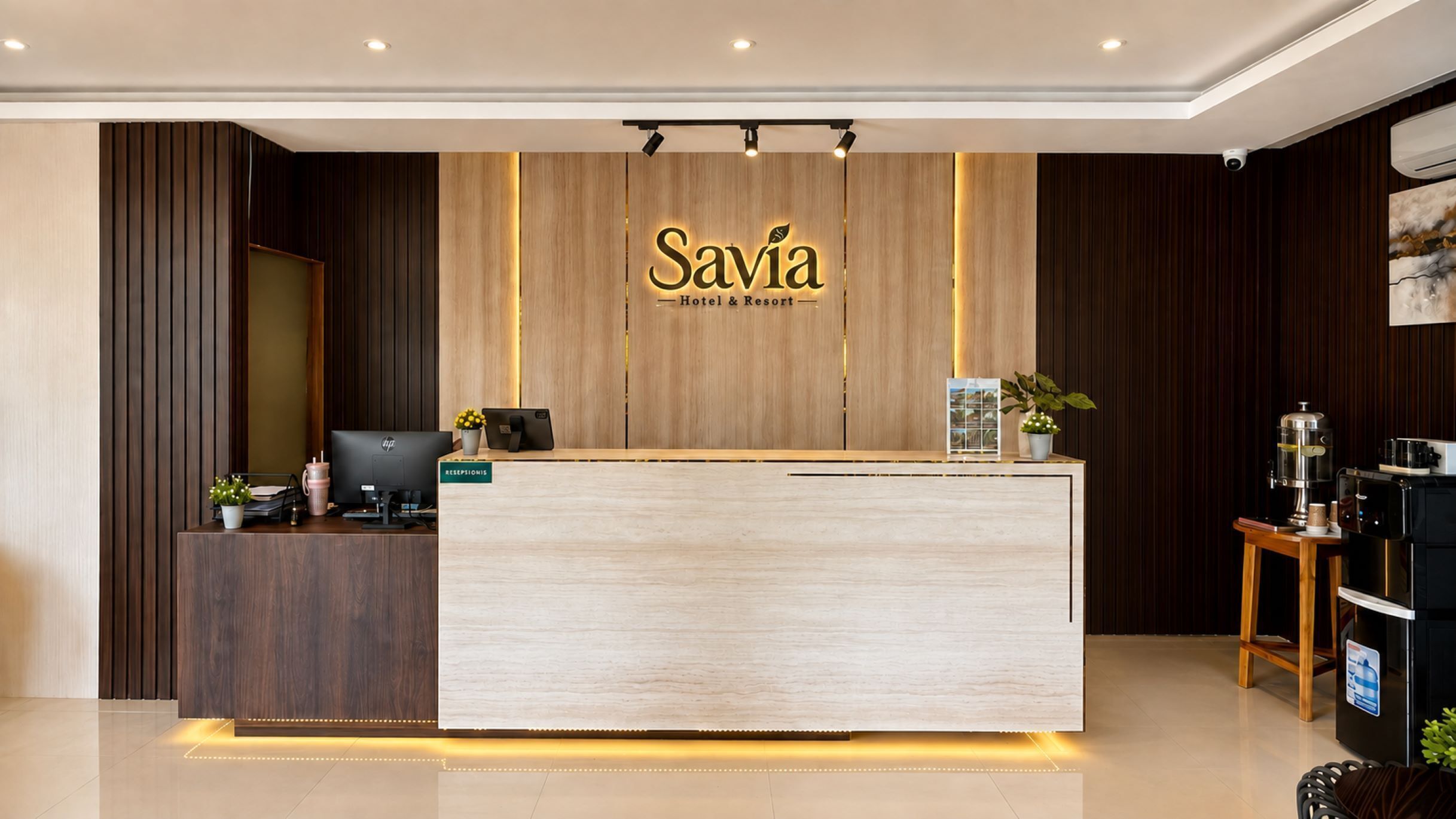 Un mostrador de recepción con terminación de madera, una pantalla digital y un letrero que dice 'Savia Hotel & Resort'.