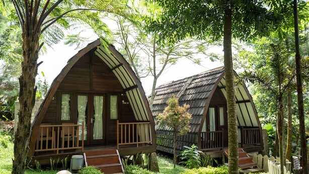 Two wooden cabins with pitched roofs, surrounded by lush greenery and a stone pathway. - Savia Hotel & Resort Ciater (Ciater)