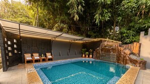A swimming pool with a tiled edge, surrounded by lounge chairs and a stone wall. - Savia Hotel & Resort Ciater (Ciater)