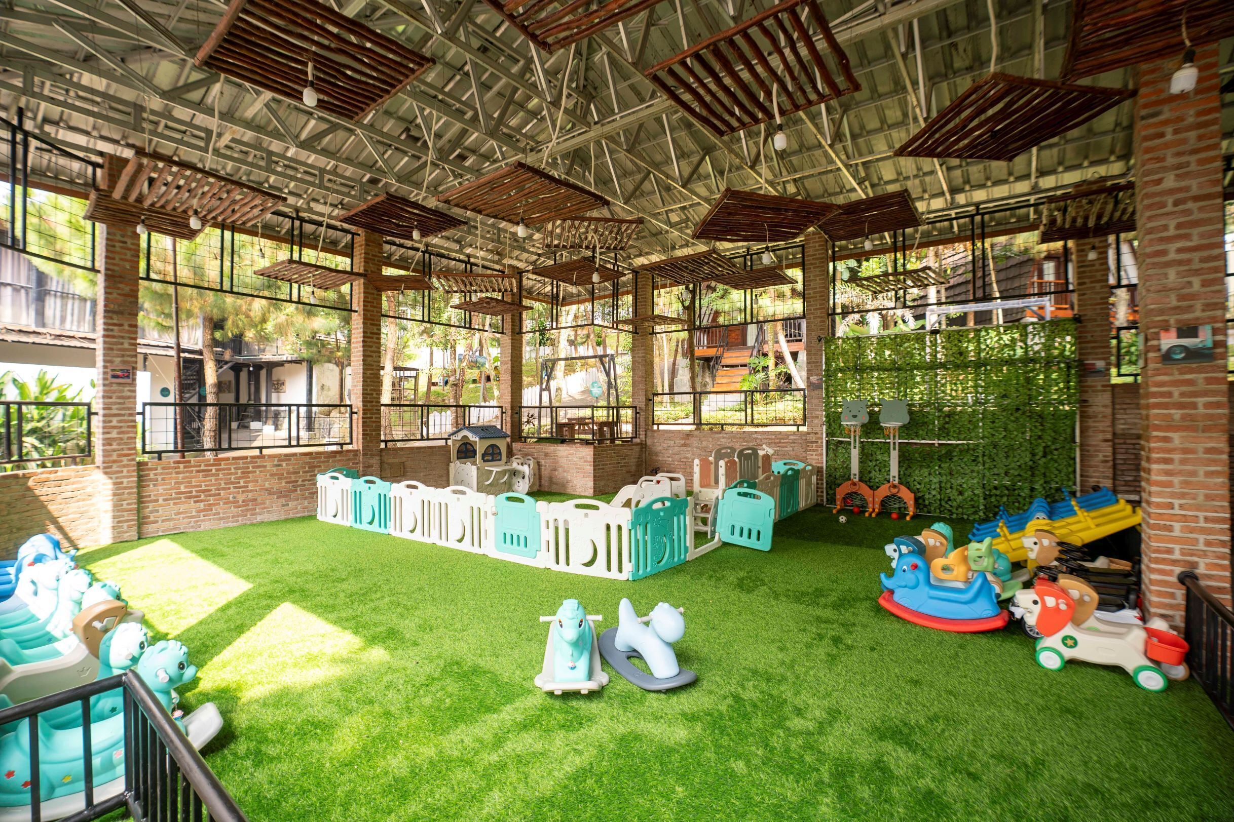 An indoor play area with artificial grass, play structures, and a brick wall.