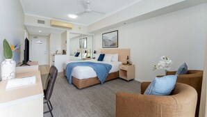 A hotel room with a bed, a desk, a chair, a nightstand, a mirror, and a ceiling fan. - Studio Escape | Views, Dining, Stadium & CBD (South Townsville)