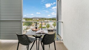 A balcony with a table, two chairs, an open book, a wine bottle, and a view of a cityscape. - Studio Escape | Views, Dining, Stadium & CBD (South Townsville)