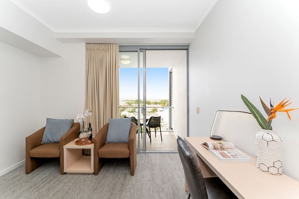 Une chambre d’hôtel moderne avec deux canapés, une petite table, un bureau et une vue sur l’extérieur, accessible par une porte-fenêtre coulissante.