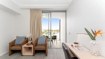 Une chambre d’hôtel moderne avec deux canapés, une petite table, un bureau et une vue sur l’extérieur, accessible par une porte-fenêtre coulissante.