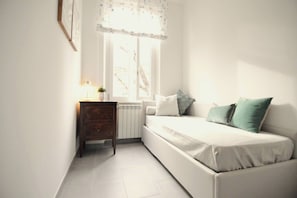 Ein Zimmer mit einem weißen Sofa, einem kleinen Holztisch, einer Heizung und einem Fenster mit Vorhang.