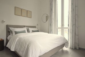 A bedroom with a bed, a bedside table, a wall-mounted mirror, and a window with curtains. - Suite Vallombrosa - Premium Apartment Near the Fonti of Fiuggi (Fiuggi)