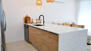 A modern kitchen with a white marble countertop, wooden cabinetry, a built-in dishwasher, and a black faucet. - Walk to Beach New Elegant 3BR with Pool  (Lower Carlton)