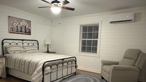 A bedroom with a bed, a chair, a window, an air conditioner, and a ceiling fan.