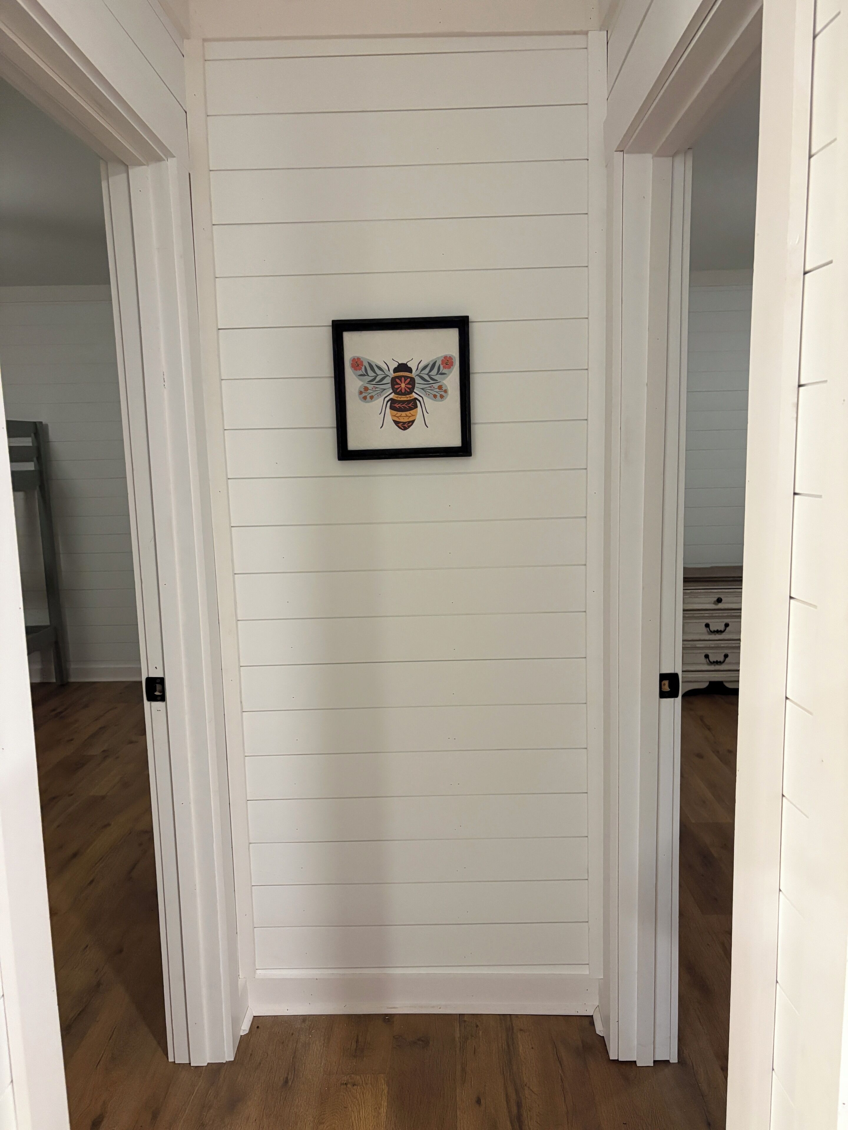 Un pasillo con paneles blancos y una obra enmarcada de una abeja en la pared.