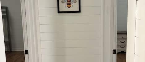 A hallway with white paneling and a framed artwork of a bee on the wall.