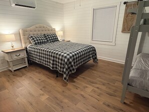A bedroom with a bed, nightstand, lamp, and wooden flooring.