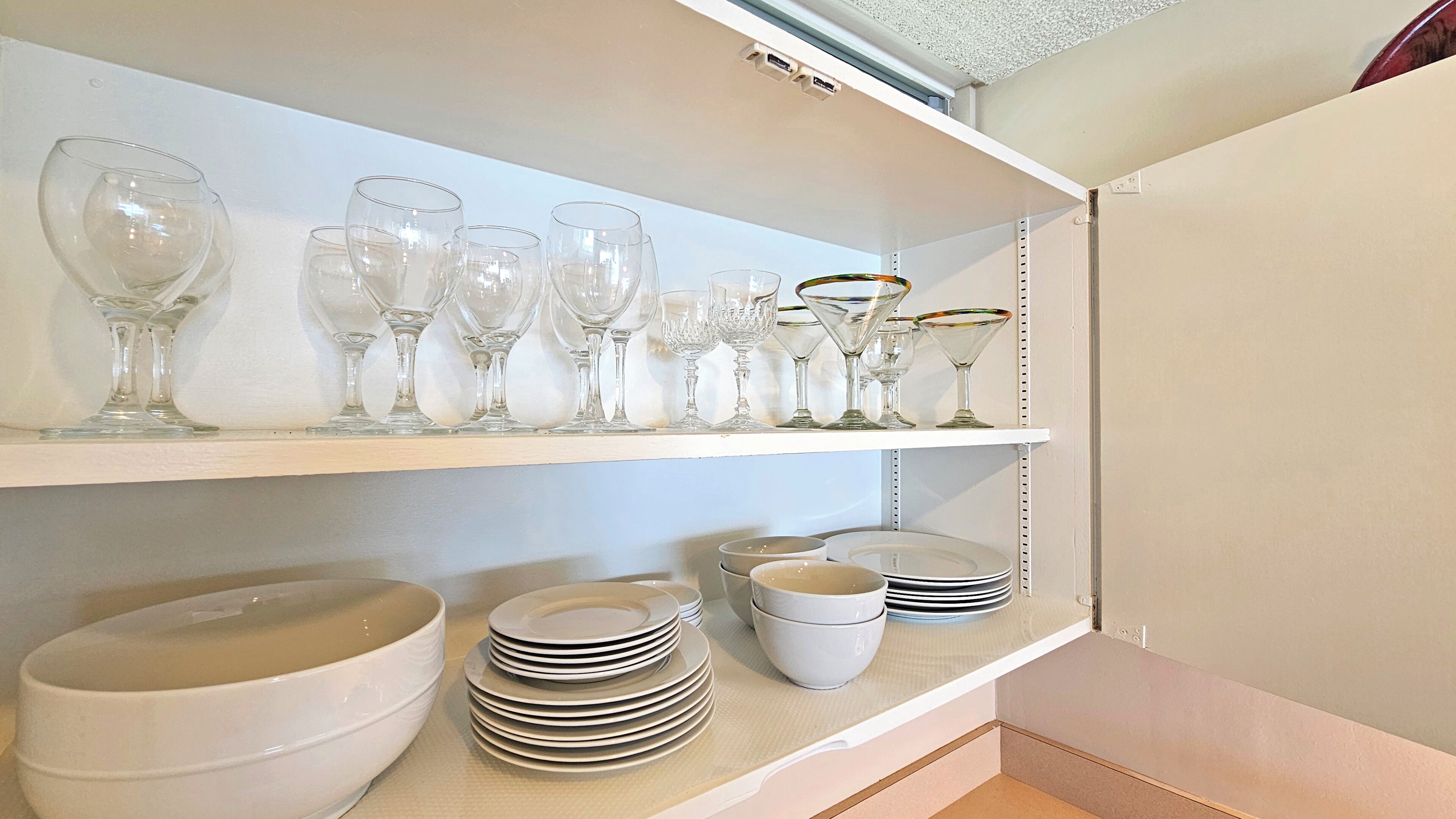 A kitchen with white shelves holding various glassware and bowls.