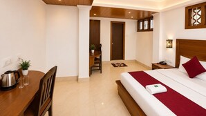 A hotel room with a wooden ceiling, a bed with a red blanket, a bedside table with a lamp, and a small desk with a chair. - Gangtok Central Rooms (Gangtok)