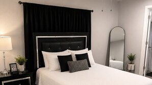 Un dormitorio moderno con una cama, mesitas de noche, un ventilador de techo, un espejo y una planta en maceta.