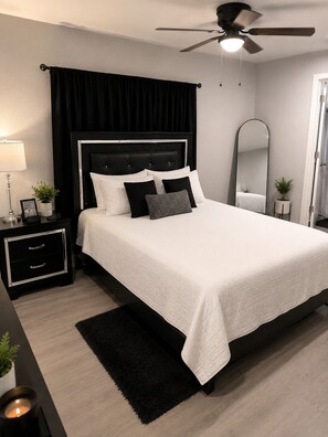 A modern bedroom with a bed, bedside tables, a nightstand, a ceiling fan, a mirror, and a potted plant. - Oakleaf Retreat | Modern 2-Bedroom Townhouse • Patio • Garage • (Oldsmar)