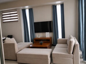 Ein Wohnzimmer mit einer Sofagarnitur, einem Couchtisch, einem Flachbildfernseher und einem kleinen Holznachttisch.
