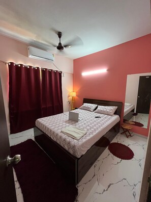 Ein Schlafzimmer mit einem Bett, einem Laptop, einer Nachttischlampe, einem Deckenventilator und einem Spiegel.