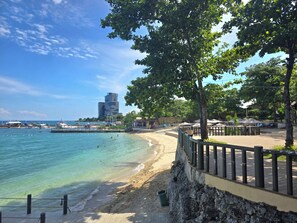 A beach with clear water, a wooden walkway, and a stone wall. - Mactan Infinity Pool View Near Airport & Beach (Lapu-Lapu)