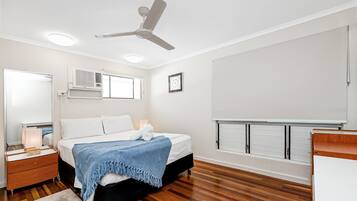 A bedroom with a bed, bedside table, nightstand, ceiling fan, and built-in storage unit.