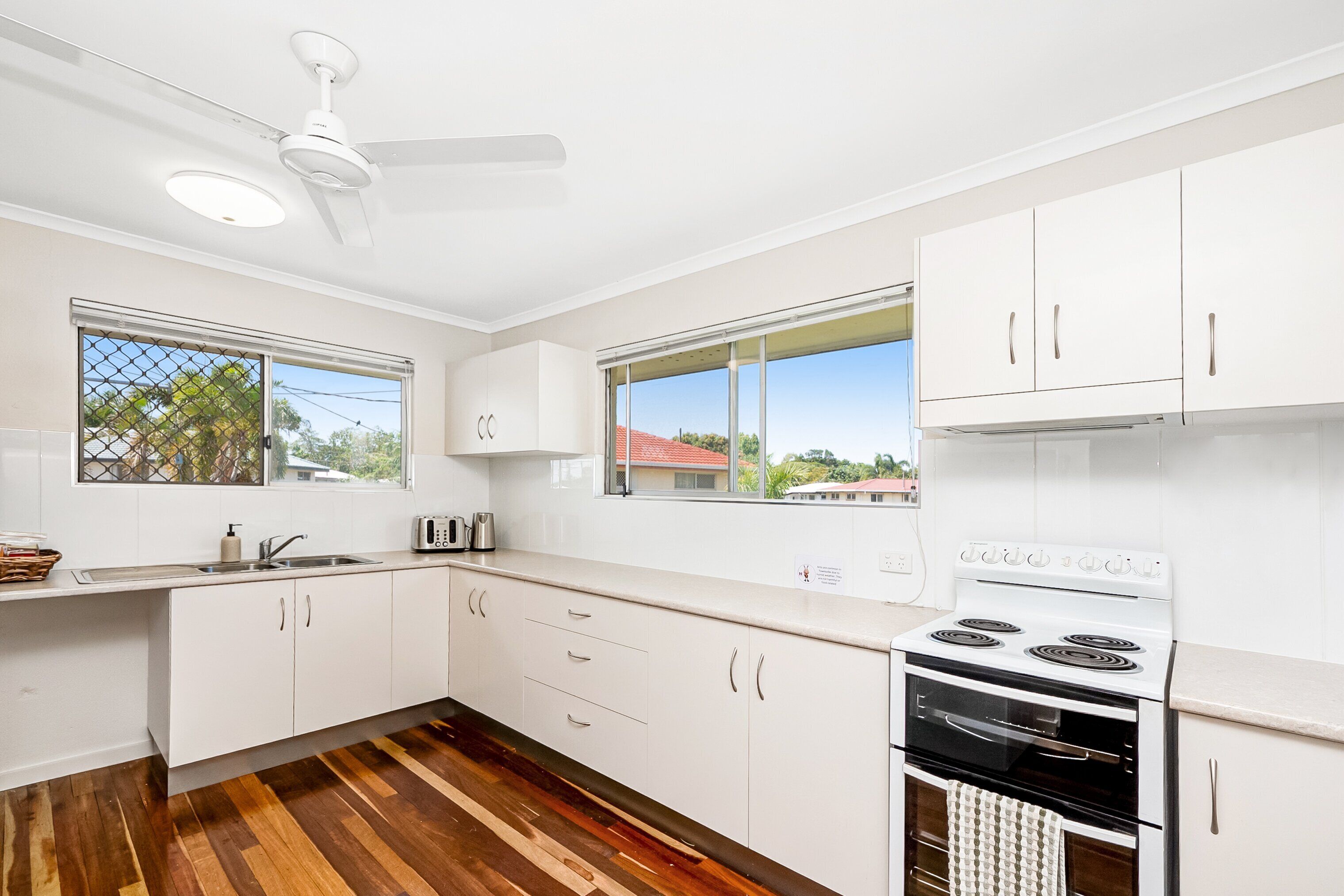 A modern kitchen with white cabinets, a stove, and a ceiling fan.