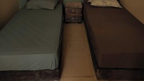 Een kamer met twee eenpersoonsbedden, een klein nachtkastje en een wandlamp.