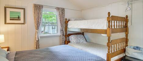 A room with a bunk bed, a single bed, a framed picture, a window with curtains, and a dresser.