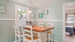 Un comedor con mesa de madera y sillas blancas, una ventana con vistas y adornos en la pared.
