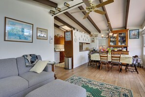 Ein Wohnzimmer mit einer Couch, einem Essbereich mit Stühlen und einem Tisch, Holzbalken an der Decke und einer Küchenzeile mit Schränken und einem Kühlschrank.
