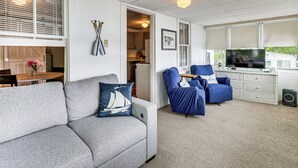 A living room with a grey sofa, a blue armchair, a television, and a kitchen in the background. - Dock & Sunset Views! Waterfront Thompson Getaway (Thompson)