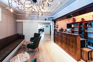 A bar area with a wooden counter, seating with a bench and chairs, and a chandelier with antlers.