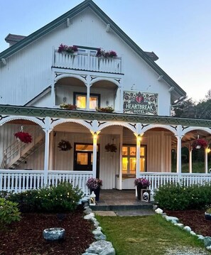 A white building with a sign reading 'Heartbreak Hotel.' It has a balcony with flowers, a porch with lights, and a staircase leading to the entrance.