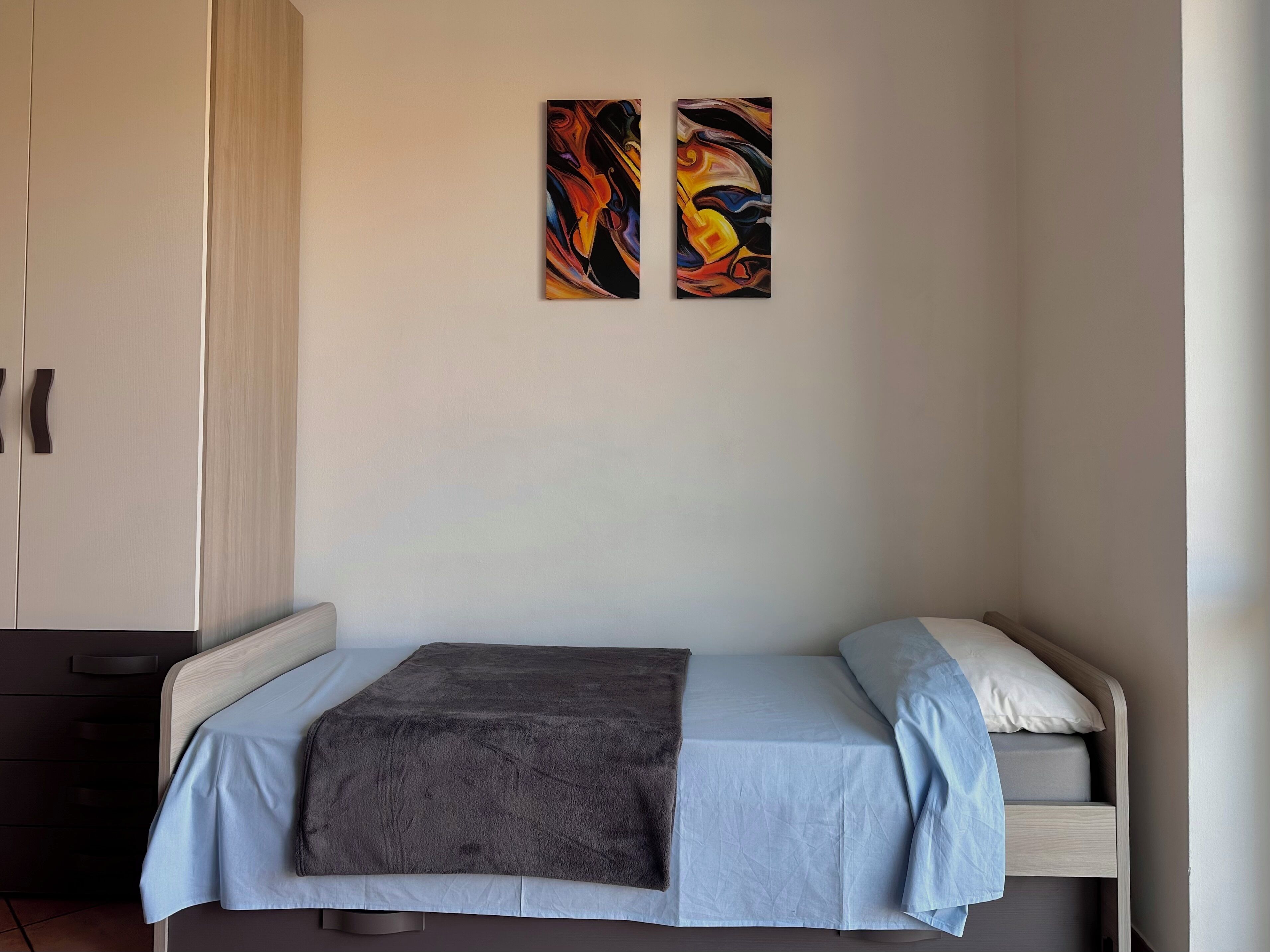 Een slaapkamer met een bed, een kledingkast en twee abstracte schilderijen aan de muur.
