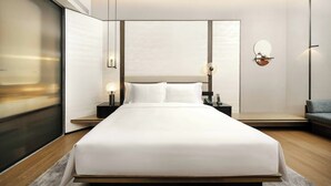 Quarto de hotel moderno com uma cama grande, mesas de cabeceira, uma luminária na parede e um sofá.