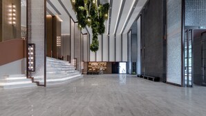 Um hall amplo com piso de mármore, escadaria, balcão de recepção e uma instalação de plantas suspensas.