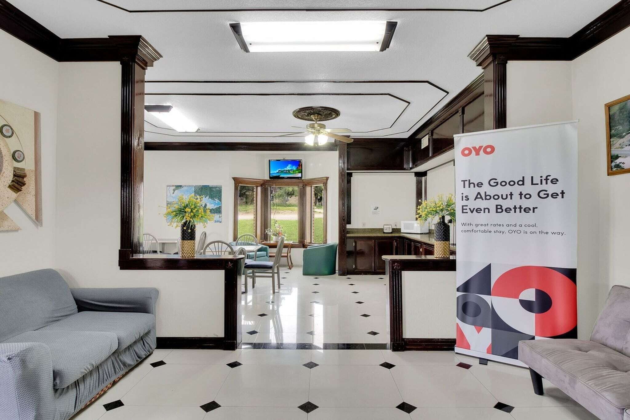 A hotel lobby with a reception desk, a television, a dining area with chairs and a table, and a large OYO advertisement.