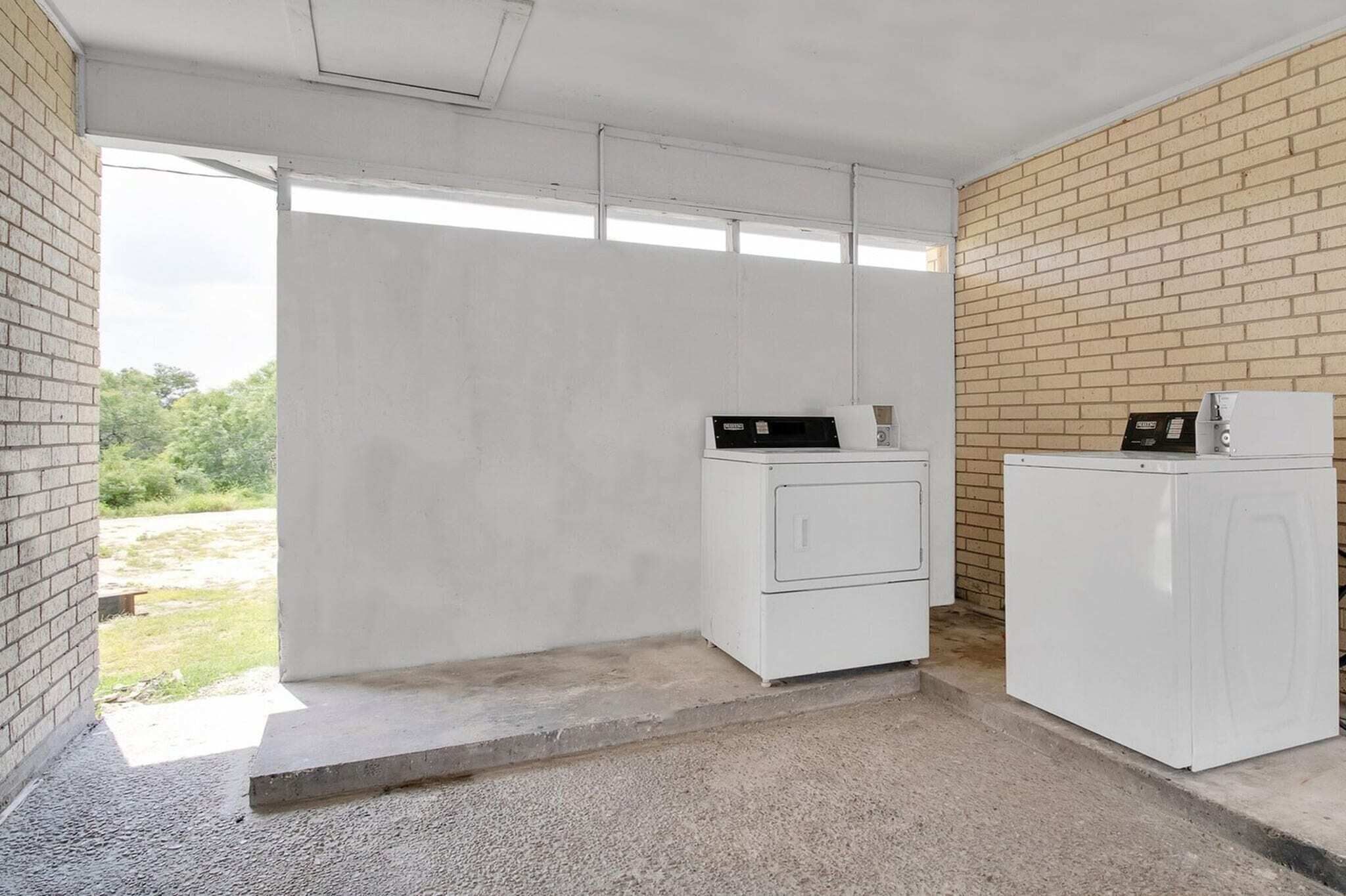 Een wasserette met twee witte wasmachines, een bakstenen muur en een betonnen vloer.