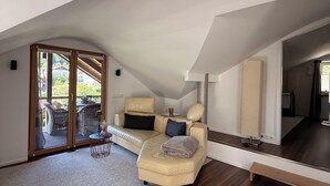 Ein modernes Schlafzimmer im Loft-Stil mit einem großen Schiebeglastür, die auf einen Balkon führt, einer gemütlichen Sitzecke mit kleinem Tisch und einem großen Spiegel, der den Raum reflektiert.