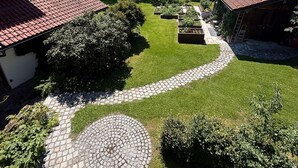 Ein Garten mit einem Kiesweg, einem runden Steinbecken und einem Backsteinhaus mit rotem Dach.