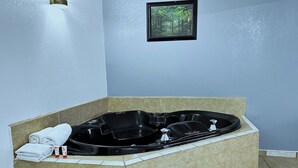 A bathroom with a black bathtub, white towels, and a framed picture on the wall. - King Bed Non Smoking (Three Rivers TX)