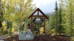 Une enseigne indiquant la présence d’un chalet, ornée d’un logo représentant une montagne, et entourée d’arbres et d’une structure en bois.