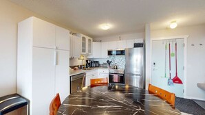 Eine kompakte Küche mit weißen Schränken, einem Edelstahlkühlschrank und einem Esstisch mit schwarzer Marmorplatte.