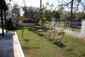 An outdoor seating area with tables and chairs, surrounded by a low fence and trees.