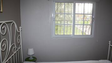 Un dormitorio con una cama individual, una ventana que da a un jardín y una mesita de noche con una lámpara.