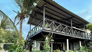 Een gebouw met twee verdiepingen, een metalen dak en een balkon, omgeven door weelderige tropische begroeiing.